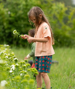 Little Green Radicals dark green blue kids organic cotton shorts with repeat apple print all worn by a child with a light orange t-shirt. 