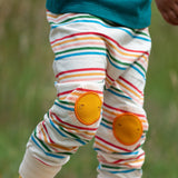 Close up of the Little Green Radicals cream rainbow striped knee patch organic cotton kids joggers being worn. The sunshine applique knee patches has embroidered details.