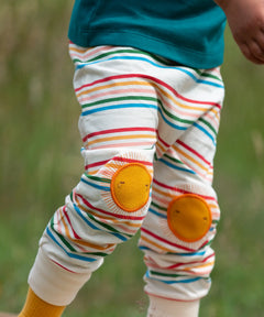 Close up of the Little Green Radicals cream rainbow striped knee patch organic cotton kids joggers being worn. The sunshine applique knee patches has embroidered details.