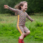 A child wearing the Little Green Radicals Vintage Flowers UPF 50+ Recycled Sunsafe Sunsuit with a pair of red wellington boots.