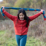 Child holding the Little Green Radicals tulips knitted blue scarf abover her head. Blue scarf with red tulips.