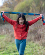 Child holding the Little Green Radicals tulips knitted blue scarf abover her head. Blue scarf with red tulips.