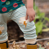 Close up of the Little Green Radicals weather knee patch blue and cream striped organic cotton joggers worn with a green apple print t-short and yellow wellington boots.