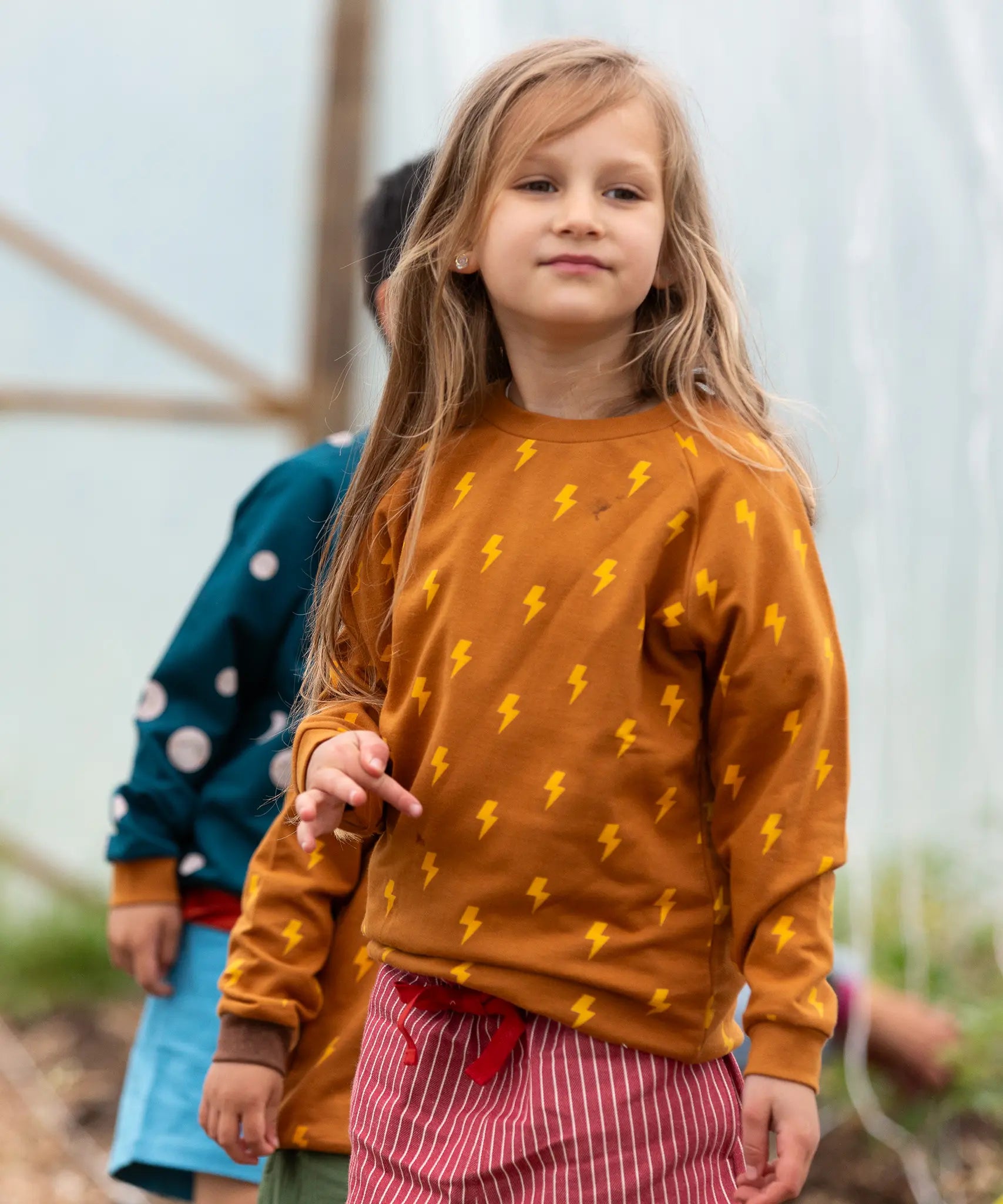 Child wearing the Little Green Radicals kids yellow lightning repeat print organic cotton sweatshirt with red pinstripe shorts.