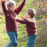 Child wearing the Little Green Radicals knitted organic cotton jumper with a mushroom Fair Isle design with green corduroy trousers.Another child is wearing a brown knitted cardigan withe corduroy trousers.