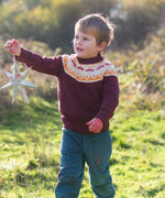 Child wearing the Little Green Radicals knitted organic cotton jumper with a mushroom Fair Isle design with green corduroy trousers. 