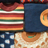 Collection of Little Green Radicals knitted wool and cotton kids jumpers shown folded.