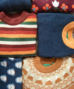 Collection of Little Green Radicals knitted wool and cotton kids jumpers shown folded.