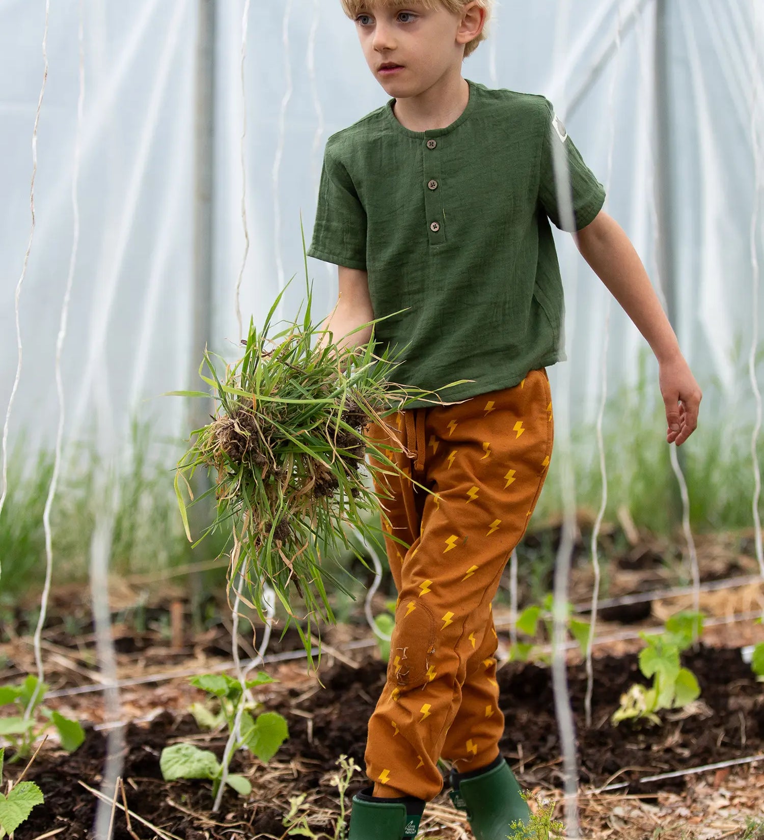 Child wearing the Little Green Radicals yellow gold repeat lightning print cosy organic cotton kids joggers with a green henley muslin t-shirt.