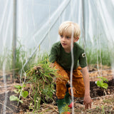 Child kneeling down wearing the Little Green Radicals yellow gold repeat lightning print cosy organic cotton kids joggers with a green henley muslin t-shirt and green and red wellington boots.