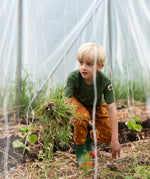 Child kneeling down wearing the Little Green Radicals yellow gold repeat lightning print cosy organic cotton kids joggers with a green henley muslin t-shirt and green and red wellington boots.