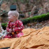 Child wearing the Little Green Radicals little unicorns organic cotton babygrow in purple sitting on a ochre yellow blanket outdoors.