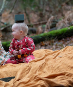 Child wearing the Little Green Radicals little unicorns organic cotton babygrow in purple sitting on a ochre yellow blanket outdoors.