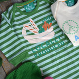 Little Green Radicals Locally Produced Playsuit placed on a wooden surface surrounded by different vegetables. An Oli & Carol Ramona The Radish Mini Doudou Baby Teether is placed on the playsuit 
