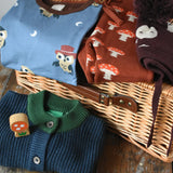 Collection of Children's clothing draped on a wicker hamper. Maxomorra owl top, mushroom knitted joggers, moon knitted hat and blue knitted cardigan. 