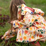 Child wearing the Little Green Radicals flower meadow recycled waterproof kids raincoat with red wellington boots.