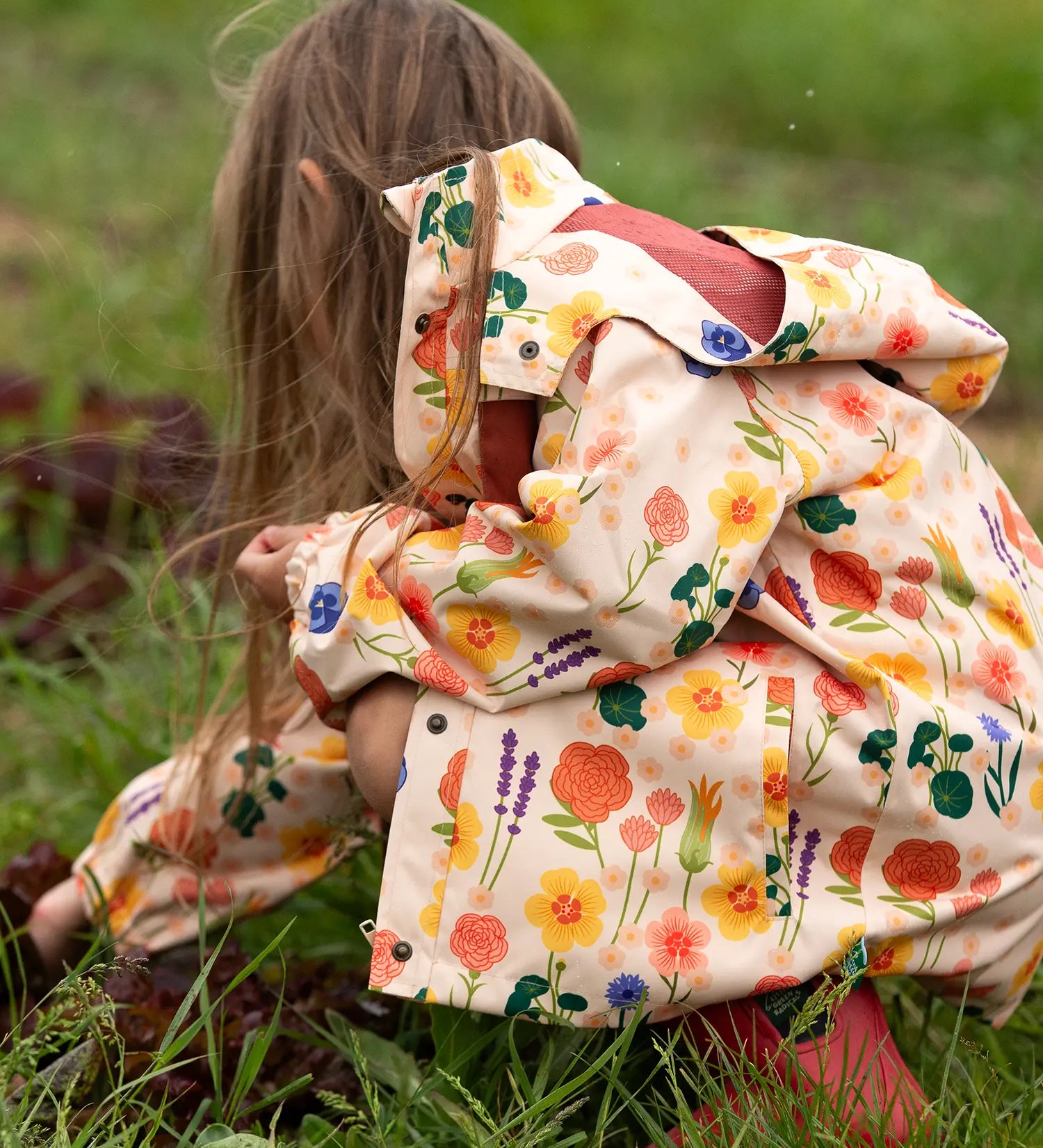 Child wearing the Little Green Radicals flower meadow recycled waterproof kids raincoat with red wellington boots.