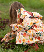 Child wearing the Little Green Radicals flower meadow recycled waterproof kids raincoat with red wellington boots.