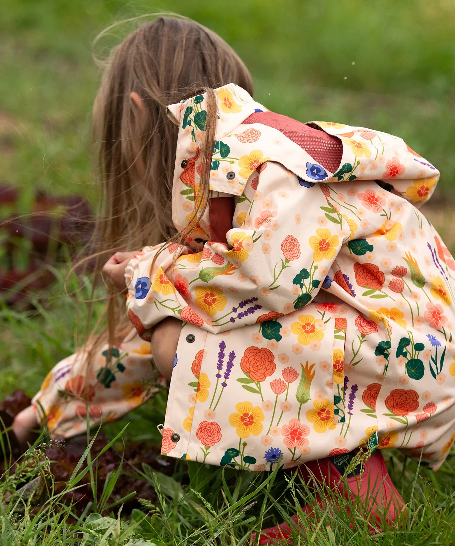 Child wearing the Little Green Radicals flower meadow recycled waterproof kids raincoat with red wellington boots.