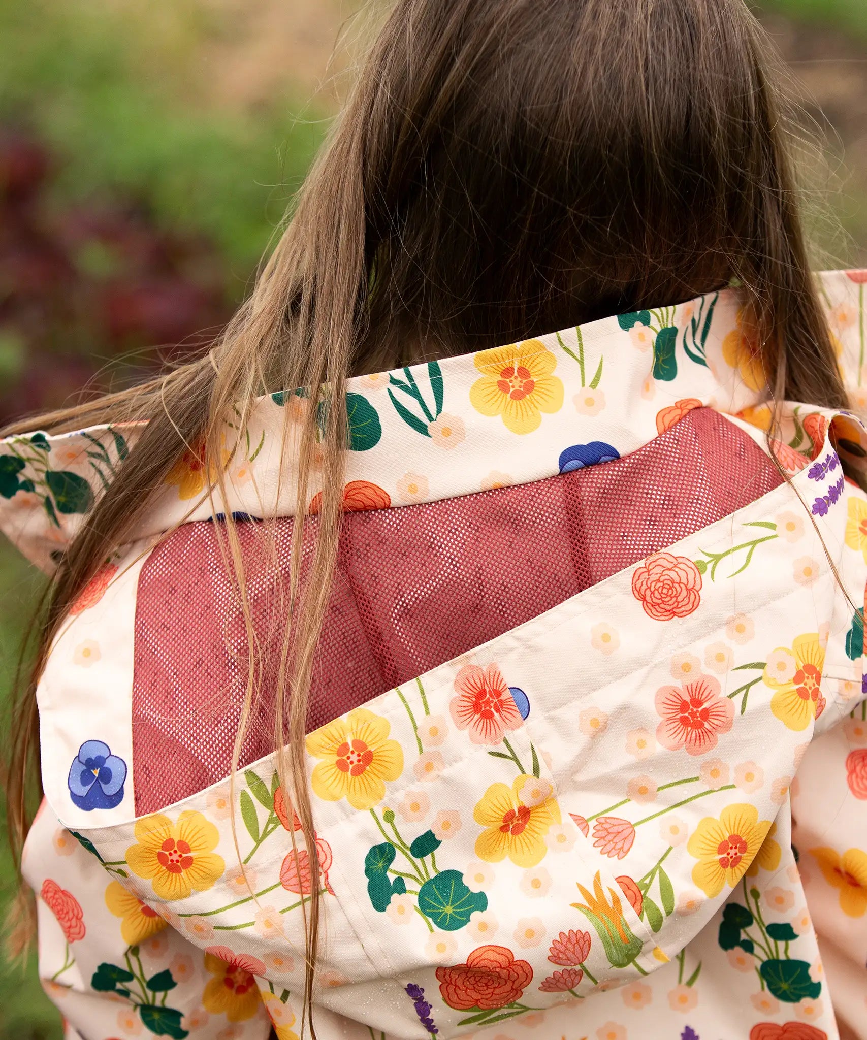 mesh lined hood on the Little Green Radicals flower meadow recycled waterproof kids raincoat with a child wearing it.