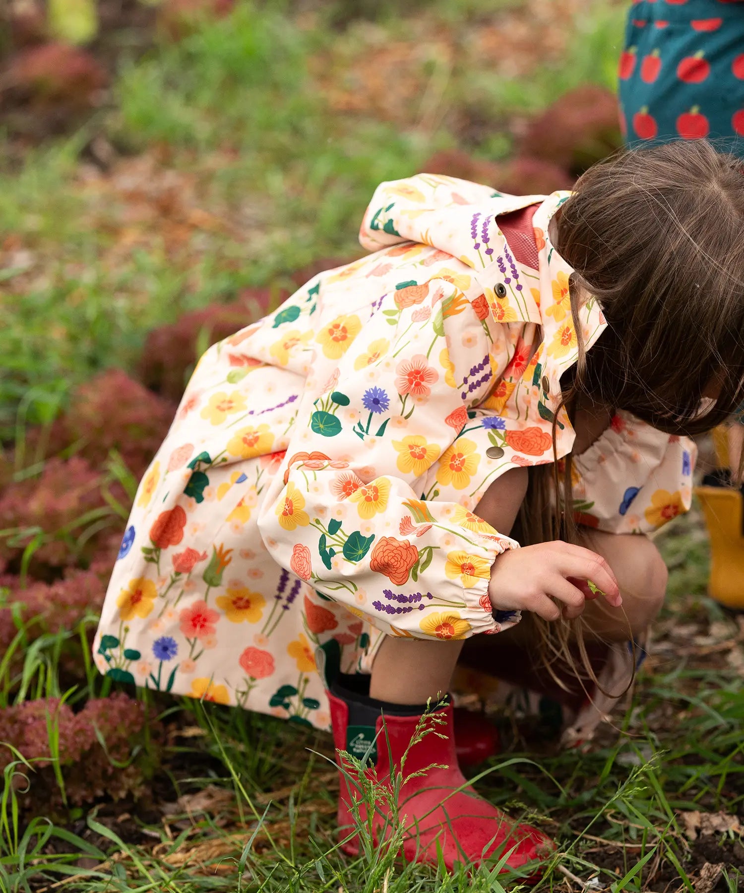 The side of a child wearing the Little Green Radicals flower meadow recycled waterproof kids raincoat.