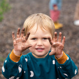 Close up of child wearing the Little Green Radicals midnight moon print blue raglan organic-cotton children's sweatshirt holding his soil covered hands up to the camera.