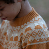 Close up of a child wearing the Little Green Radicals mountain Fair Isle snuggly woollen jumper in yellow gold. The Fair Isle details n around the neckline featuring snow topped mountains surrounded by patterns.