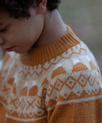 Close up of a child wearing the Little Green Radicals mountain Fair Isle snuggly woollen jumper in yellow gold. The Fair Isle details n around the neckline featuring snow topped mountains surrounded by patterns.