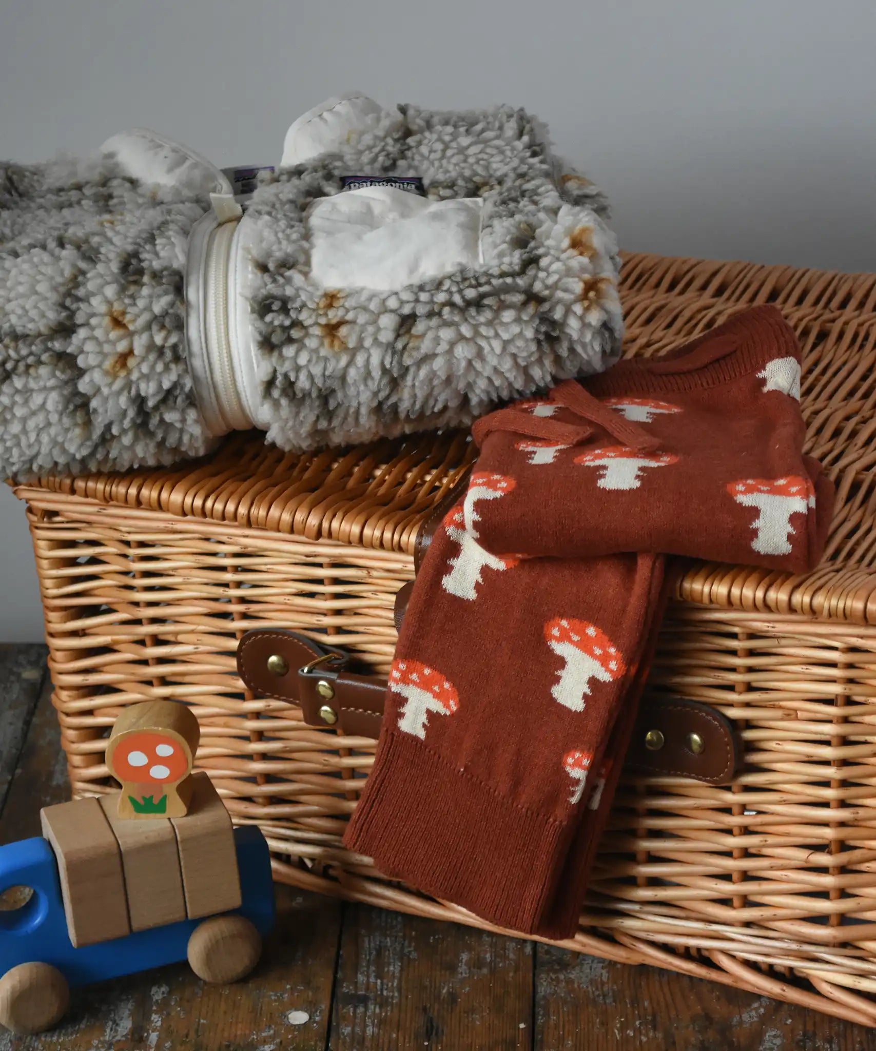 Little Green Radicals mushroom organic cotton knitted joggers placed on a wicket hamper with a Patagonia fleece in the background.