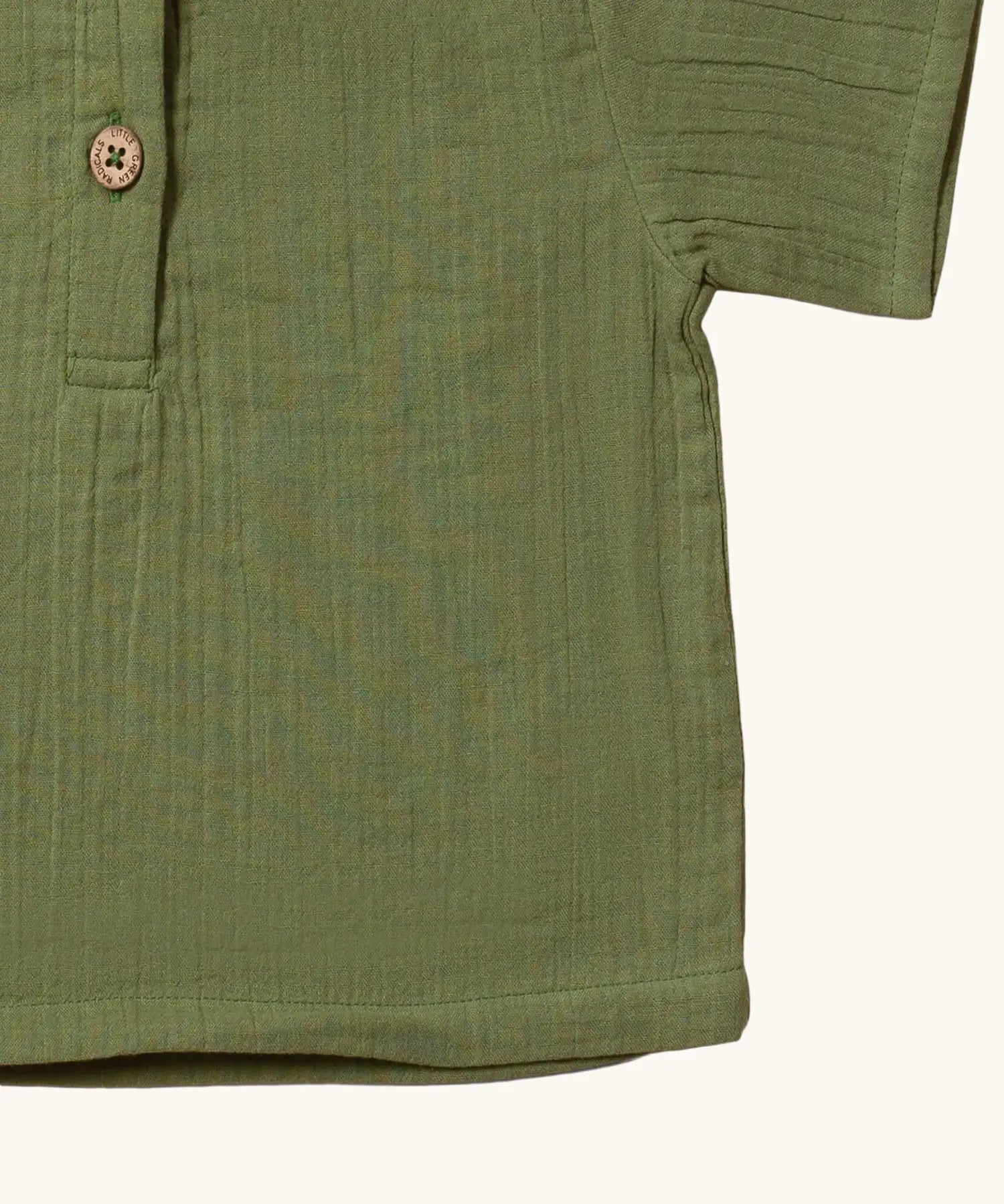 Close up of the hemline on the Little Green Radicals Muslin Loose Fit Short Sleeve Henley Top in a  Chive Green colour way.