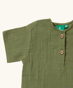 Close up of the button closure on the neckline of the Little Green Radicals Muslin Loose Fit Short Sleeve Henley Top in a Chive Green colour.
