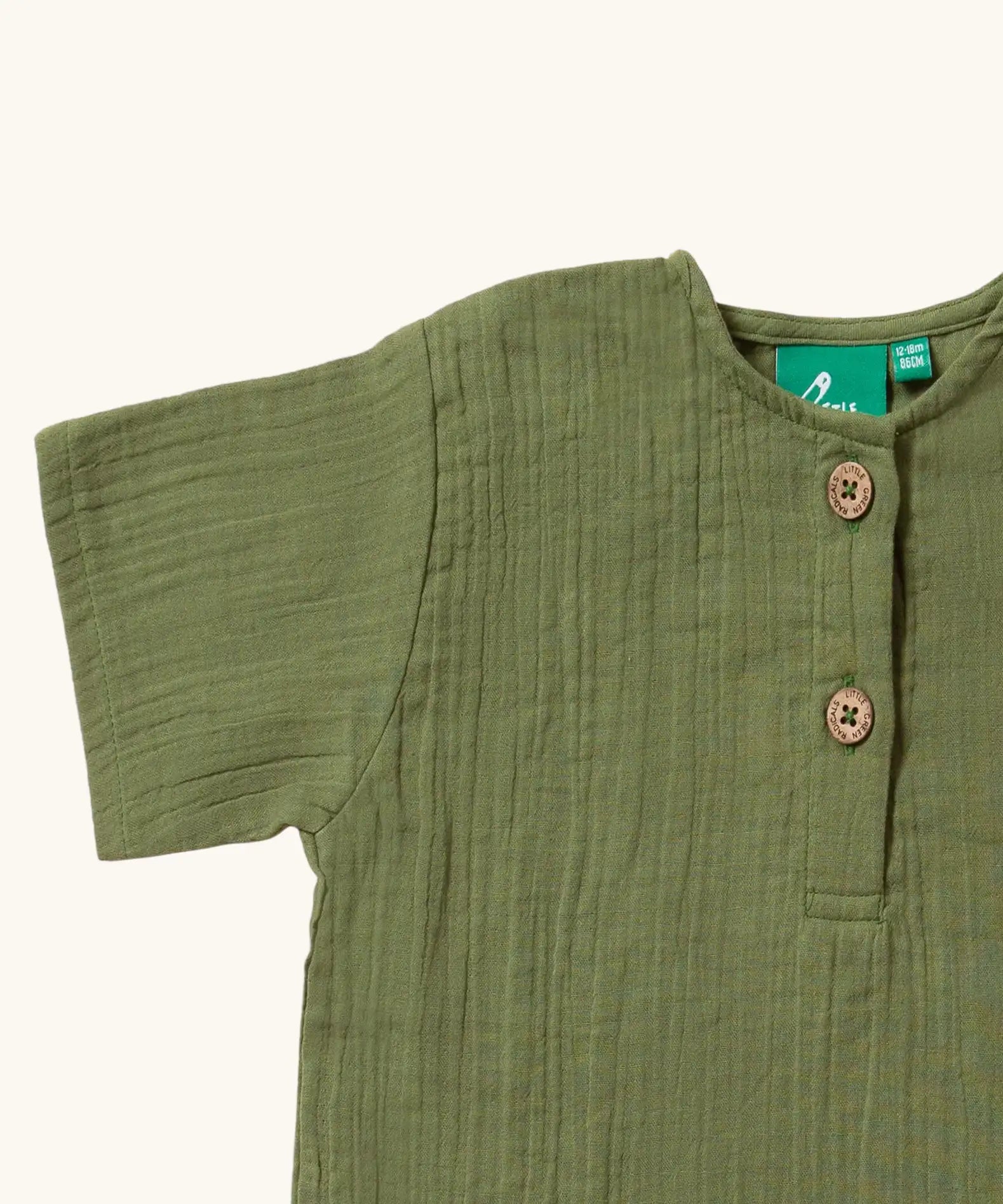 Close up of the button closure on the neckline of the Little Green Radicals Muslin Loose Fit Short Sleeve Henley Top in a Chive Green colour.