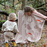 Child standing behind a Little Green Radicals cream folk tales knitted organic cotton baby blanket that they are holding up in front of them.