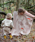 Child standing behind a Little Green Radicals cream folk tales knitted organic cotton baby blanket that they are holding up in front of them.