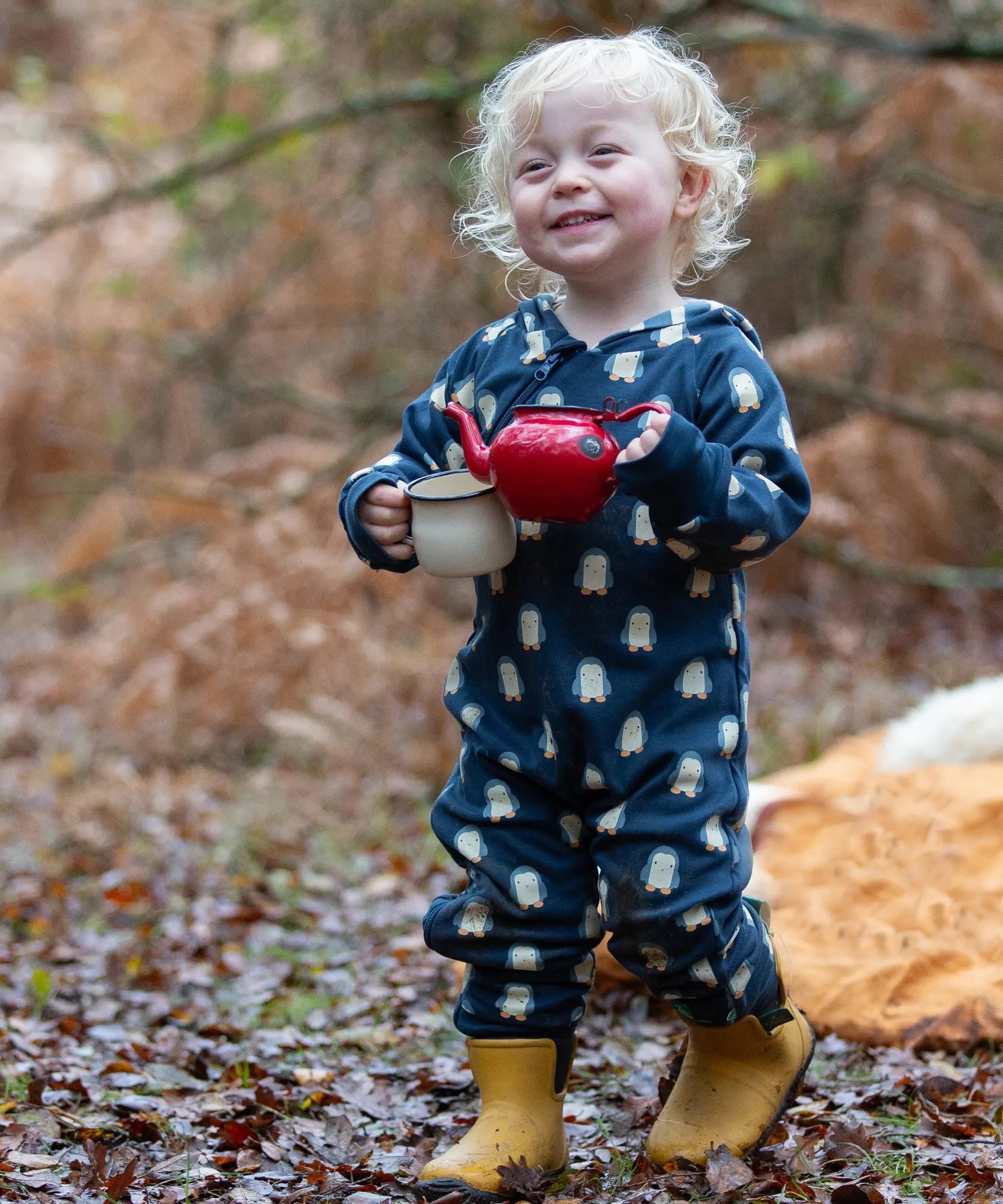 Child wearing a Little Green Radicals navy blue penguins hooded reversible snug suit with yellow gold ankle wellington boots. 