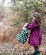 Child holding a Little Green Radicals  olive green check organic cotton stocking wearing a purple dress and green wellington boots.