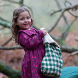 Child holding a Little Green Radicals  olive green check organic cotton stocking wearing a purple dress.