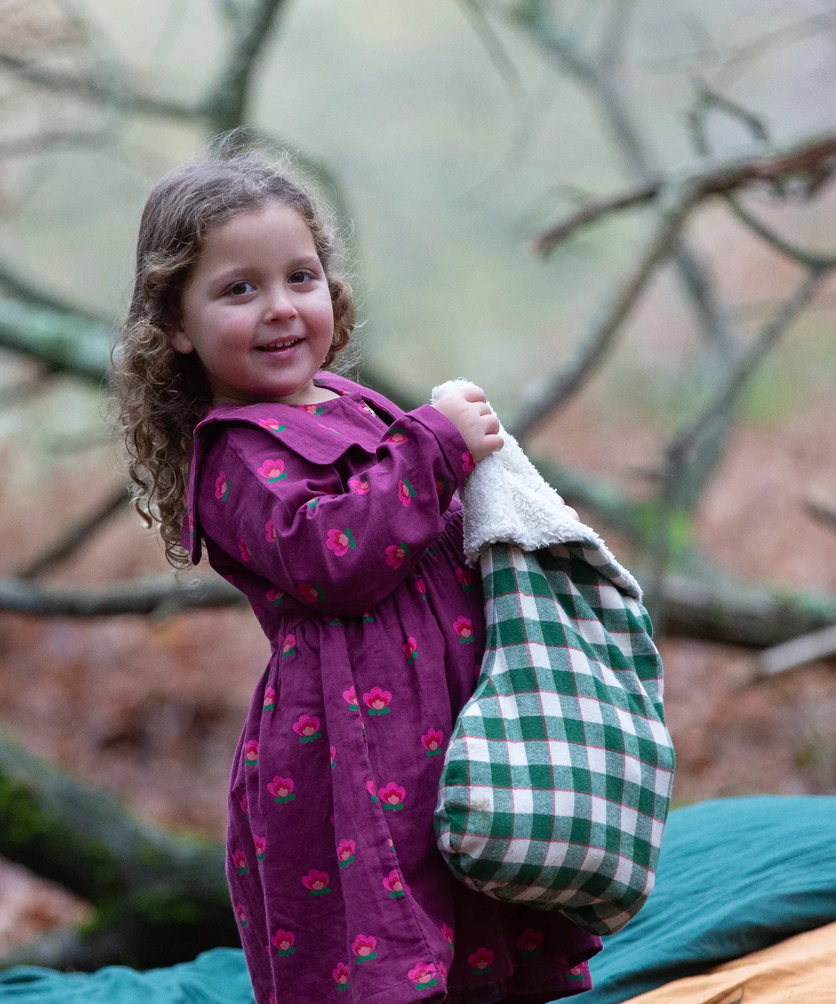 Child holding a Little Green Radicals  olive green check organic cotton stocking wearing a purple dress.