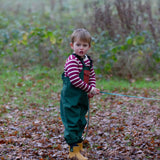 Child wearing a Little Green Radicals olive green recycled lined waterproof dungarees with a striped top underneath and yellow gold ankle wellingtons.