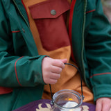 Child wearing a Little Green Radicals olive green recycled waterproof 3 in 1 coat with yellow waterproof dungarees underneath.