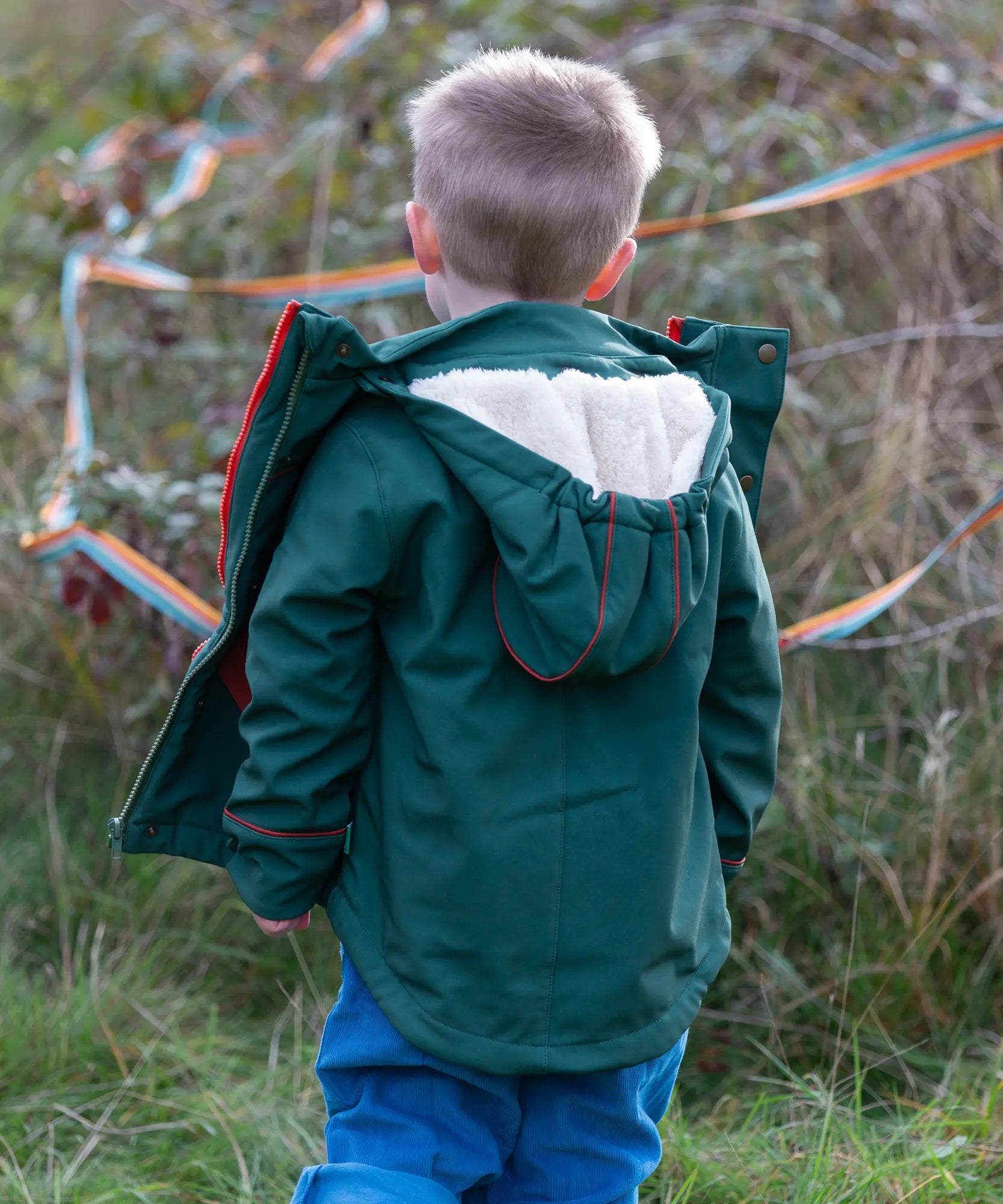 Back of a child wearing a Little Green Radicals olive green recycled waterproof 3 in 1 coat with blue corduroy trousers.
