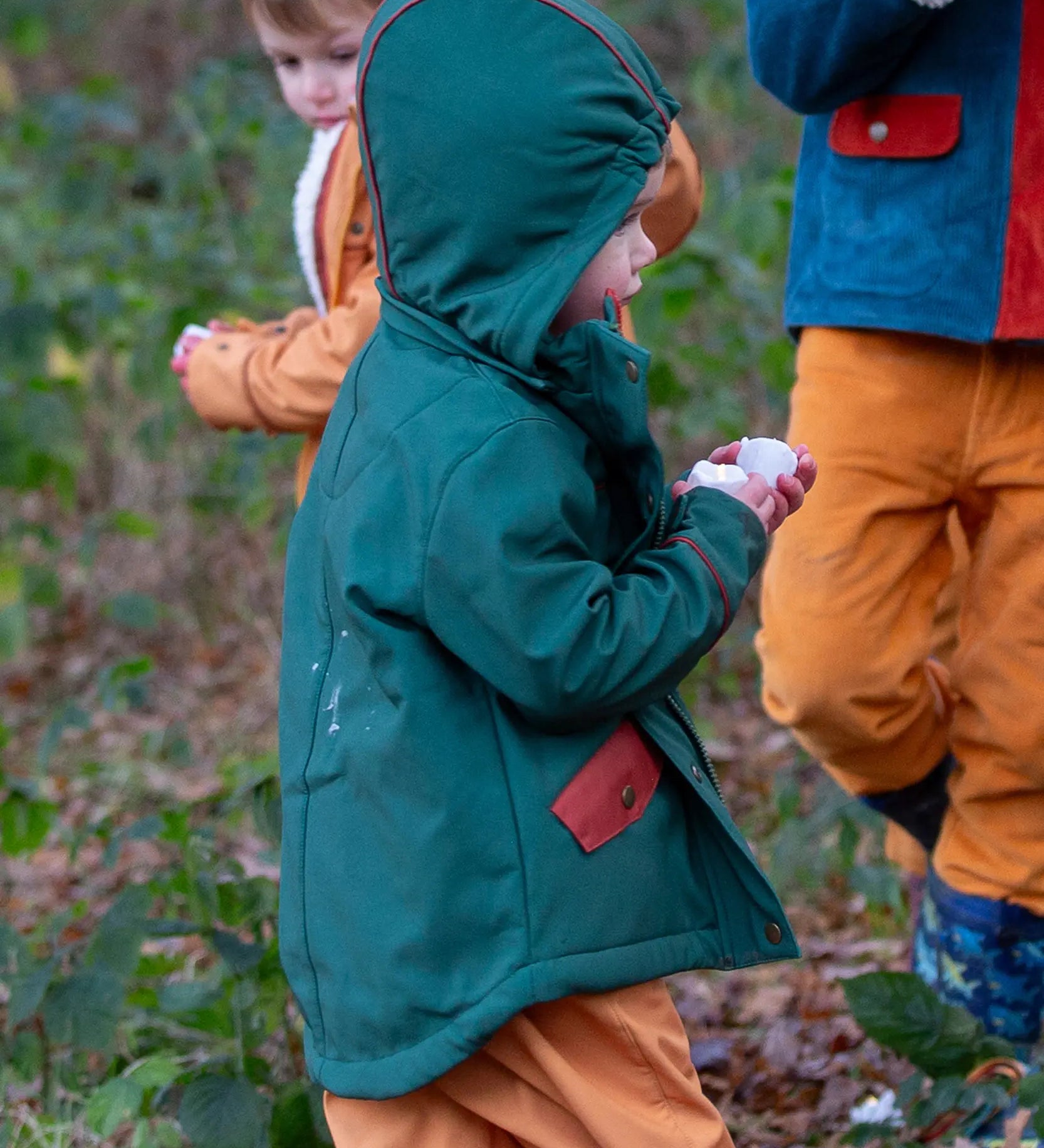 Child wearing a Little Green Radicals olive green recycled waterproof 3 in 1 coat with yellow waterproof dungarees underneath.