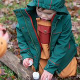 Child wearing a Little Green Radicals olive green recycled waterproof 3 in 1 coat with yellow waterproof dungarees underneath.
