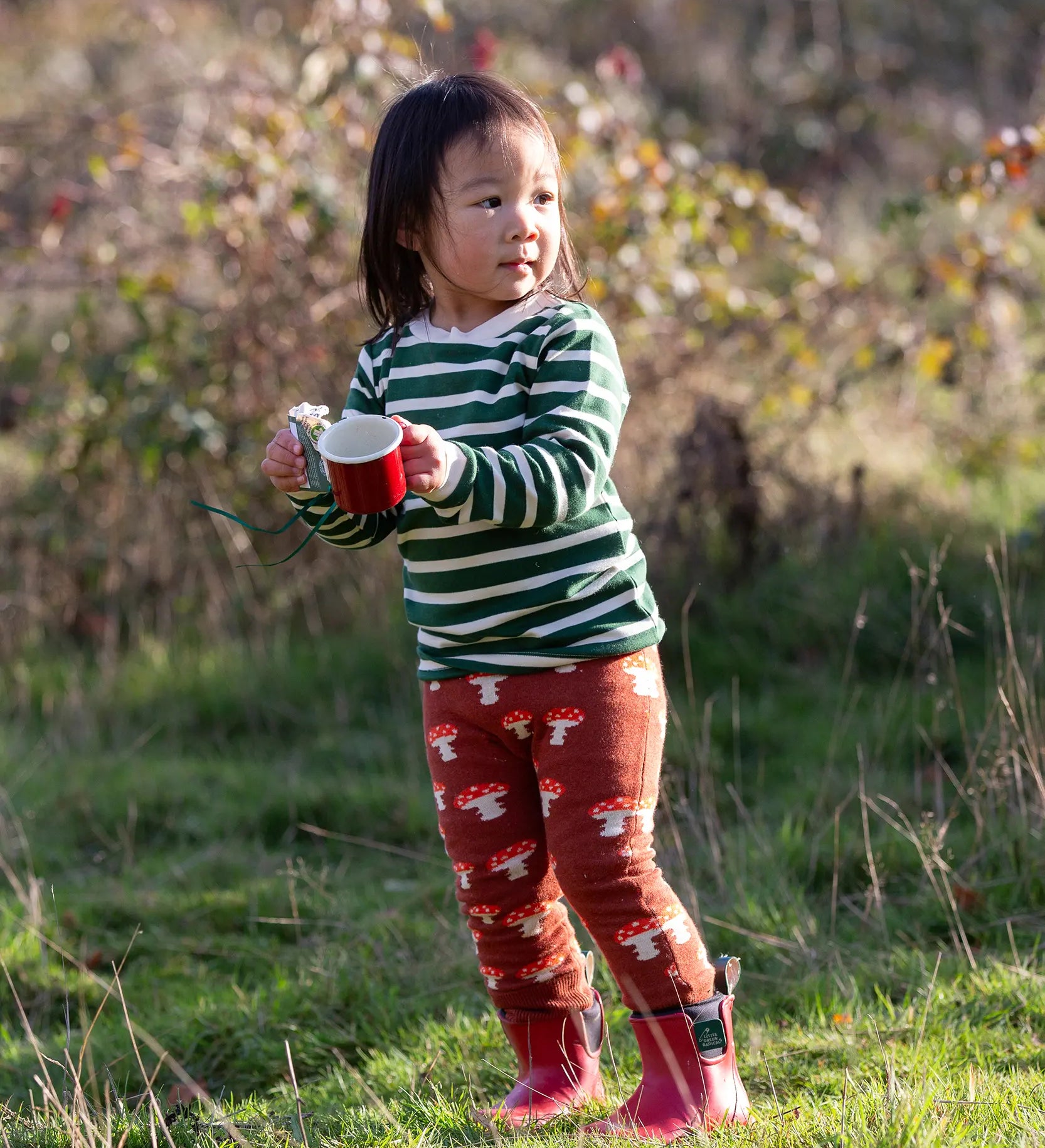 Child wearing the Little Green Radicals olive green striped long sleeve top with knitted mushroom joggers.