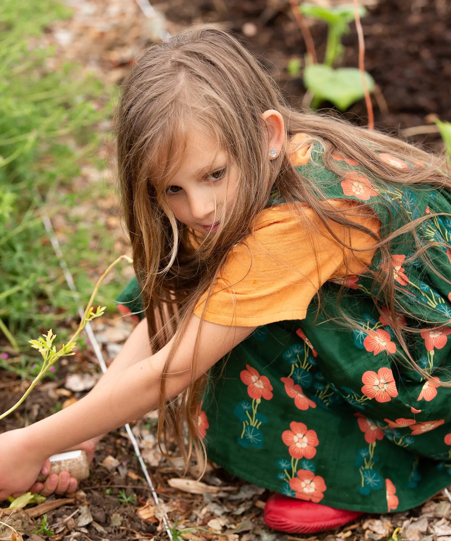 Little Green Radicals green orange blooms repeat print reversible pinny kids dress being worn with a yellow t-short underneath and red wellington boots.