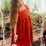 Little Green Radicals reversible organic cotton pinny kids dress shown with the orange side being worn with a yellow t-shirt underneath.
