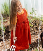 Little Green Radicals reversible organic cotton pinny kids dress shown with the orange side being worn with a yellow t-shirt underneath.