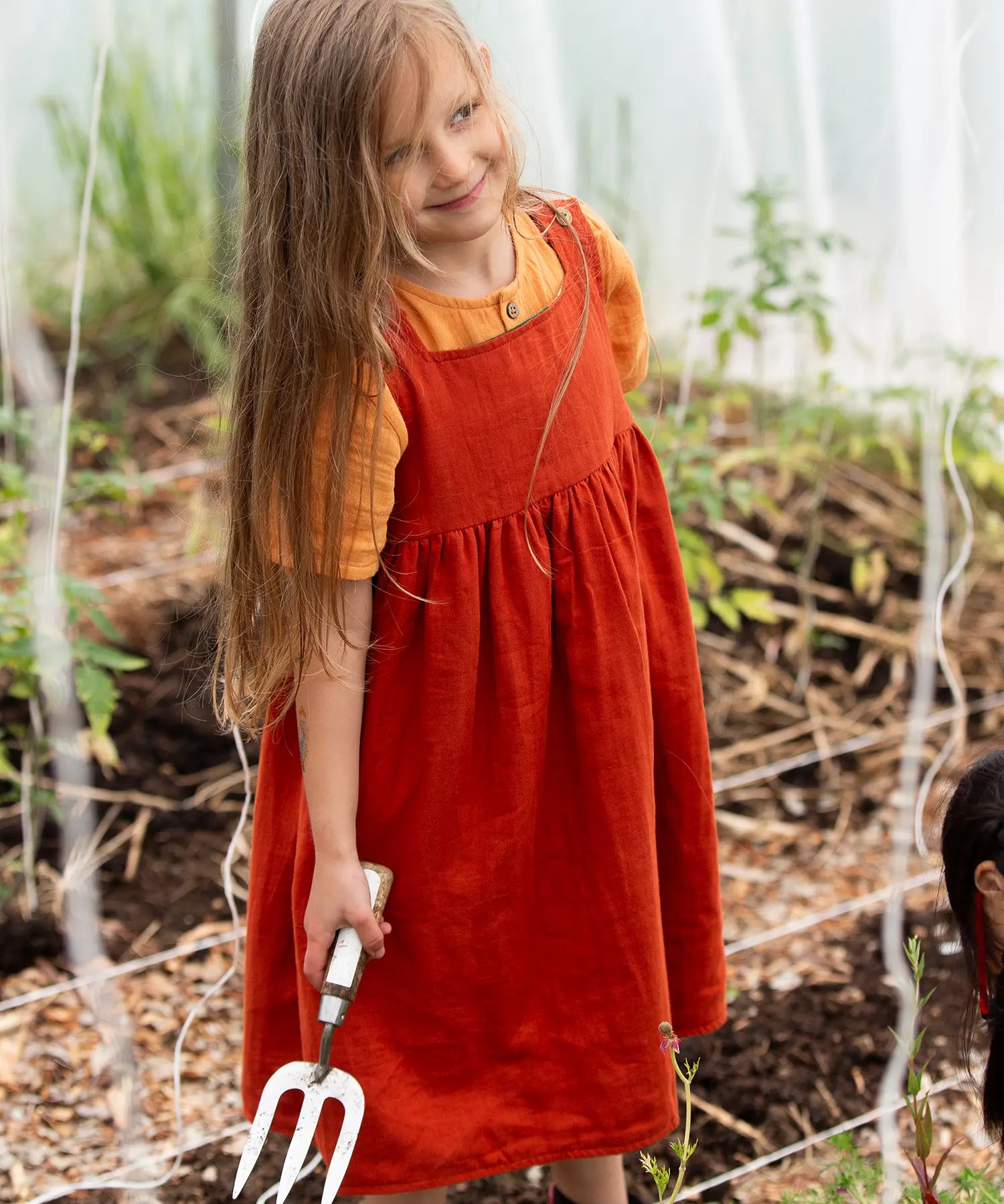 Little Green Radicals reversible organic cotton pinny kids dress shown with the orange side being worn with a yellow t-shirt underneath.