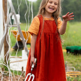 Little Green Radicals reversible organic cotton pinny kids dress shown with the orange side being worn with a yellow t-shirt underneath by a child gardening.