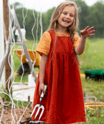 Little Green Radicals reversible organic cotton pinny kids dress shown with the orange side being worn with a yellow t-shirt underneath by a child gardening.